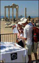 Біля розвалин стародавнього храму на березі річки Сіде у Туреччині туристи роздивляються футболки, виготовлені з нагоди сонячного затемнення
