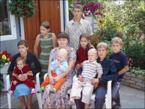 На стульях сидят 15-летняя Ольга с годовалой сестренкой Настей, 27-летняя Неонила Гага с сыном Сашей, 1 год,  13-летний Леонид с трехлетним Владом. За ними стоят 11-летняя Наталья, 16-летний Александр, 9-летняя Юля и шестилетний Эдуард