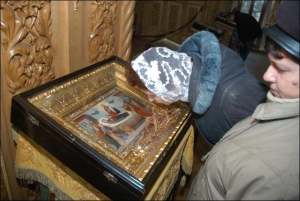Посетительница церкви Всех Преподобных Святых в Киевской Лавре целует икону Успения Богородицы, в которой на сухой веточке лилии выросли живые листики 