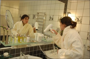 Дівчина, яка відповідає за розміщення гостей у новому готелі ”Опера”, показує ванну кімнату. Постояльцю готель пропонує набір шампунів і кремів. На дівчині халат, який можна купити за 800 гривень