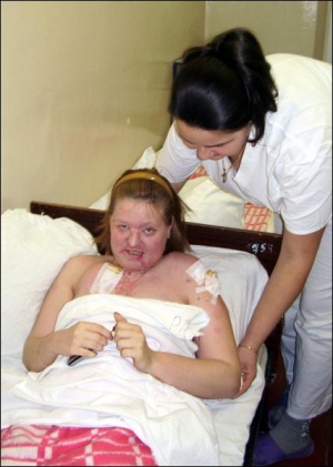 Медсестра Київського центру пластичної хірургії Олена Негель допомагає облитій кислотою Тетяні Вороніній підвестися на ліжку. В руках мобілка, на яку регулярно телефонує її кривдник
