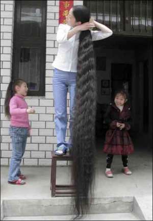 Китаянка Ксі Айфенґ розчісує волосся на порозі свого будинку у місті Кіангсі. Миття голови та розчісування займає півтори години, бо волосся у жінки 2 м 42 см завдовжки