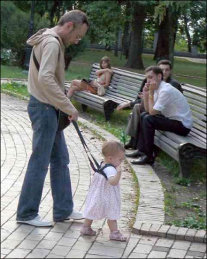 Отец поддерживает дочь с помощью детских вожжей в Мариинском парка Киева