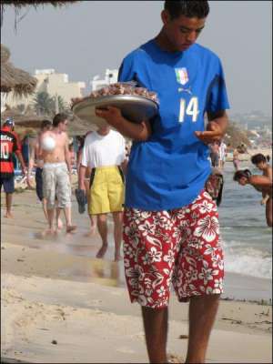 На пляже возле гостиницы ”Роял Жинен” в тунисском городе Сусс парень продает миндаль в какао по 2 доллара за пакетик