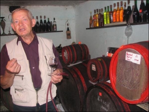 Винороб Іван Урста тримає у своєму підвалі кілька бочок домашнього вина. Келихи для дегустації наповнює з гумового шланга