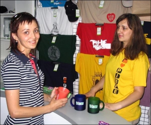 Продавець сувенірного кіоску в центрі Рівного Світлана Чеславська (праворуч) показує Тетяні Маковській чашки з назвою міста. Жінка вибирає сувеніри на подарунок синові, який гастролює з молодіжним танцювальним ансамблем