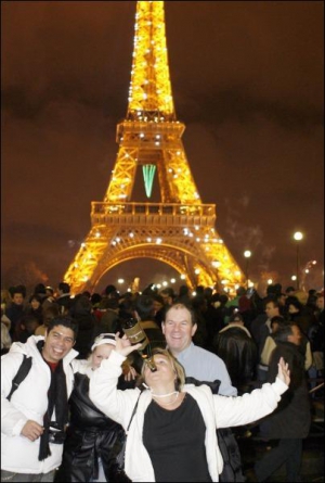 Туристи святкують Новий рік біля Ейфелевої вежі у Парижі. Увечері навіть у будній день там збирається багато приїжджих, щоб подивитися на нічну вежу у вогнях