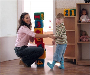 Артем грається з вихователем Наталією Педенко у садочку №662. Хлопчик вибирає кубик потрібного кольору і ставить його на верх піраміди