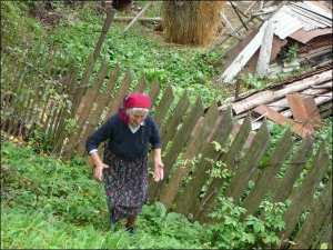 Пенсіонерка з села Пасічна Надвірнянського району Катерина Остап’юк показує, як під дією зсувів зменшилася ділянка біля її хати й нахилився паркан