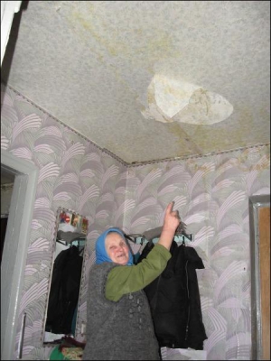 Пенсионерка Ксения Адаменко показывает подтеки, оставшиеся от воды на потолке и стенах ее квартиры в райцентре Щорс Черниговской области. Обои размокли и местами поотпадали