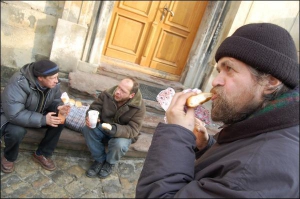 Бездомный 37-летний Виктор Михайлив (справа) с приятелями едят борщ и пампушки с чесноком на ступенях Доминиканского собора во Львове. Об угощении мужчины узнали от волонтеров, которые раздают бесплатные обеды в городе