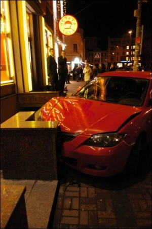 Посетители ”Мистера Снека” на Контрактовой площади рассматривают в пятницу вечером красную ”Мазду-3” у входа в кафе. Фото сделано через час после наезда на парковщика
