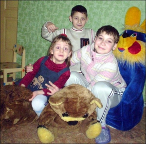 Надежда Башметова (справа) обнимает 3-летнюю Полину Моцну. Позади девочек брат Полины Иван. Дети живут в центре опеки ребенка ”Возрождение” в городе Лубны на Полтавщине, играются в дочки-матери
