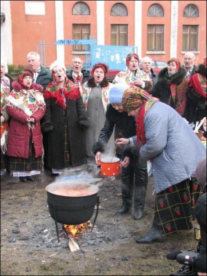 Повар Надежда Герасименко (на переднем плане справа) угощает борщом, который она сварила на улице в 30-литровом котле. Рядом поют артисты из группы ”Калина”