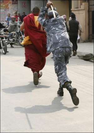 Полицейский преследует буддийского монаха во время разгона демонстрации в столице Непала Катманду. Из города Лхаса акции протеста распространились по другим регионам