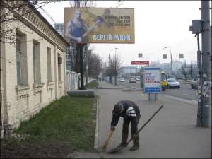 Дворник убирает тротуар на Воздухофлотском просп. возле бигборда с рекламой заместителя мэра Сергея Рудыка