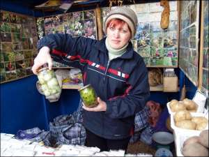 Покупцям насіння Оксана Джус показує зразки — консервовані білі огірки. На лотку Центрального ринку Вінниці жінка тримає понад десяток банок із консервованими овочами нових сортів
