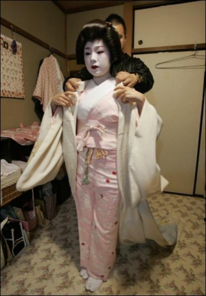 Ассистент помогает гейше Комомо одеть кимоно. У актрисы - традиционный макияж — выбеленое лицо, красные щеки, подведенные губы