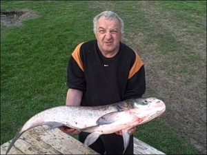 Сумчанин Володимир Стещенко тримає мертву рибину, яку витяг із води на Голубих озерах. Чоловік каже, що товстолобик важить не менше 20 кілограмів