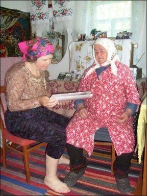 Соціальний робітник Ганна Яременко із Малих Канівець Чорнобаївського району читає газету підопічній Ганні Мелашенко. З магазину принесла бабусі хліб і кілька булочок