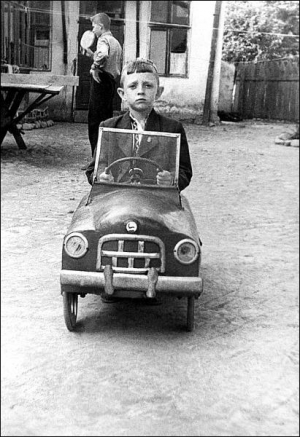 1954 год. Ефим Герасимчук на день рождения получил в подарок от отца деревянную машину. Он сидит в ней во дворе своего дома по ул. Первомайской в Виннице. Позади него соседские ребята играют в теннис