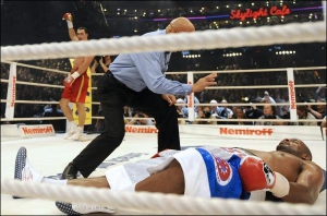 Тони Томпсон лежит на полу после удара Владимира Кличко. На счет ”девять” он поднимется, но рефери поединка Джо Кортес остановит бой. На заднем плане Кличко поднимает руку, празднуя победу