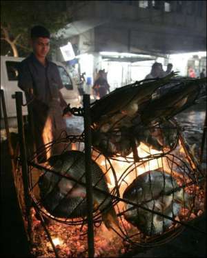 В столице Ирака Багдаде мужчина на улице жарит и сразу продает рыбу