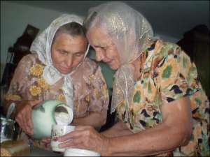 Емілія Сінгалевич у своїй хаті в Заліссі на Тернопільщині наливає кисле молоко в чашку, яку тримає сестра Марія Сушник
