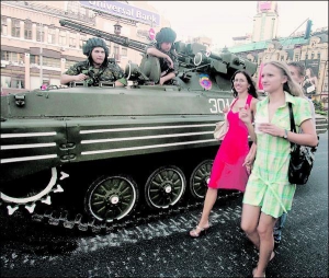 Киевлянки идут во вторник вечером мимо бронетехники на Бессарабский площади в центре столицы. На асфальте видны белые следы от гусениц