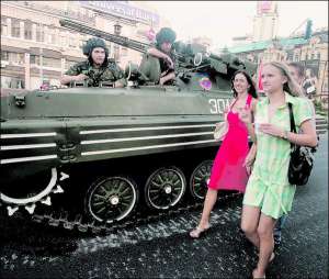 Киевлянки идут во вторник вечером мимо бронетехники на Бессарабский площади в центре столицы. На асфальте видны белые следы от гусениц