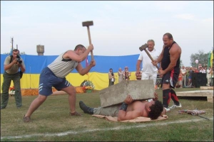 Двое мужчин разбивают на груди 29-летнего Дмитрия Халаджи 300-килограммовую бетонную плиту во время праздника богатырской силы в селе Красеновка Чернобаевского района
