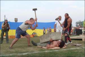 Двое мужчин разбивают на груди 29-летнего Дмитрия Халаджи 300-килограммовую бетонную плиту во время праздника богатырской силы в селе Красеновка Чернобаевского района