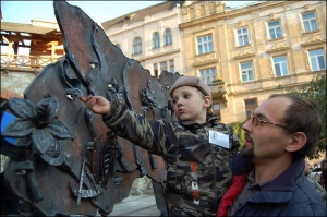 Данік Поляков із батьком чіпляють кованого змія на пластину у формі Львівської області на площі біля музею ”Арсенал” у Львові