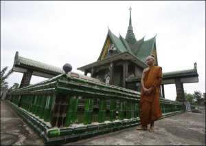Буддійський монах Сан стоїть на фоні храму з пляшок у таїландській провінції Сісакет. Усередині святині є скляні мозаїки із зображенням Будди