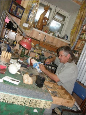Анатолий Молдаван в мастерской ремонтирует куклу Снегурочку. На подоконнике стоит деревянный дракон — это первая вырезанная из дерева игрушка Анатолия
