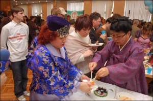 Кореянка угощает посетителей фестиваля кухонь национальным суши. Его приготовили из огурцов и крабовых палочек