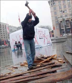 Участник акции ”Геть усіх!” рубит дрова для ”буржуйки|”, возле которой греются люди на площади Независимости в Киеве