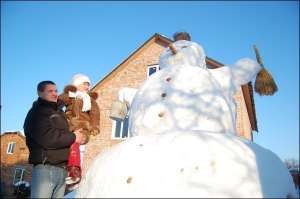 Роман Порицкий держит на руках дочку Юлию возле собственноручно слепленного  снеговика на своем дворе в селе Пидбирцы Пустомитивского района на Львовщине