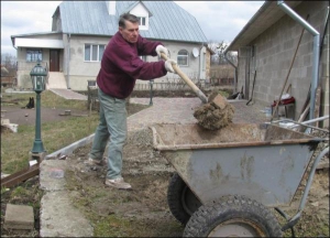 Колишній депутат Верховної Ради України Роман Омельчук насипає у тачку  пісок біля свого будинку у місті Рівному. Щоб зекономити на майстрах, кластиме бруківку від гаражу до воріт самотужки 