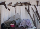 Возле старого сарая выставлен огородный реманент: грабли, тяпки, лопать