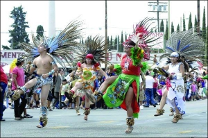 Участники праздничного парада танцуют в костюмах мексиканских индианцев на бульваре Сезара Чавеса в Лос-Анджелесе