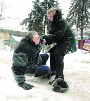Женщина помогает подняться своему мужчине, который упал на покрытый толстым слоем льда тротуаре в Киеве