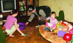 Полтавчанка Наталья Слинько с дочерью Ириной вычерпывает талую воду из комнаты в частном доме на Подоле. На диване сидит внучка хозяйки Мария