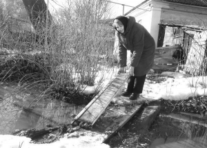 Дар’я Присяжнюк кладе дерев’яний місток, щоб пройти до туалету. Жінка боїться впасти в метрову яму, яку вимили стокові води