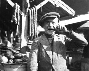 Львовский батяр перед фотокамерой ”играет варьята” — прикидывается дурачком — возле раскладки с колбасой на одном из городских базаров, 1920-ые