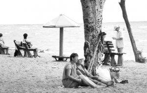 Дворники сидят под деревом на городском пляже ”Левобережный”. Его считают наилучшим в Мариуполе. Рядом расположен отстойник комбината ”Азовсталь”. Вода в море — черная