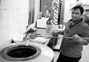 Помічник шеф-кухаря Моган Сінгх у металевій печі випікає паляниці. Їх індуси їдять замість хліба