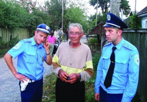 Інспектор з дізнання Гніванського відділу ДАІ у Вінницькій області Богдан Цимбалюк (ліворуч) та дільничний інспектор міліції Гніванського міського відділення стоять разом із врятованим ними Василем Кудирком. Поряд — будинок Кудирка у селі Селище Тиврівськ