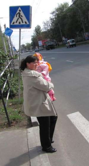 Женщина с ребенком в понедельник стоит на пешеходном переходе на улице Калинина в Полтаве. Большинство водителей на ”зебре” не притормаживают. Знак перед переходом наклонился