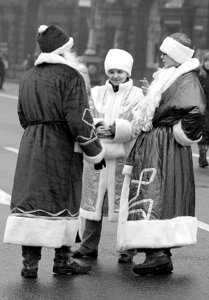 Чоловік у костюмі Діда Мороза та дві жінки-Снігуроньки стоять на столичному майдані Незалежності в суботу